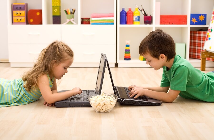 Two kids using laptops with bowl of popcorn