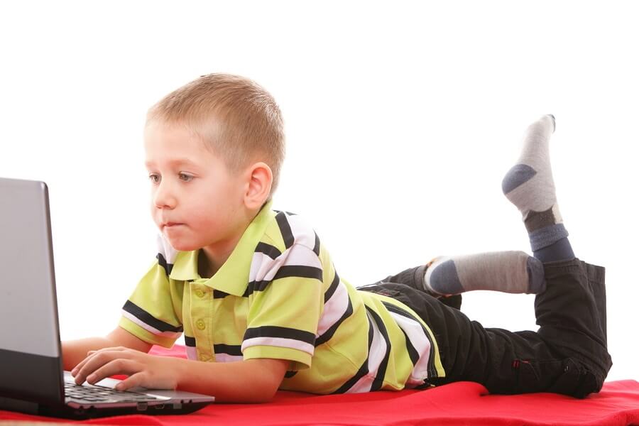 Young boy laying on stomach playing with computer