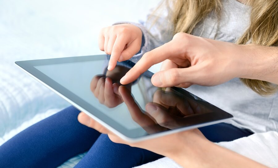 Close up of tablet with parent and child's hands in foreground