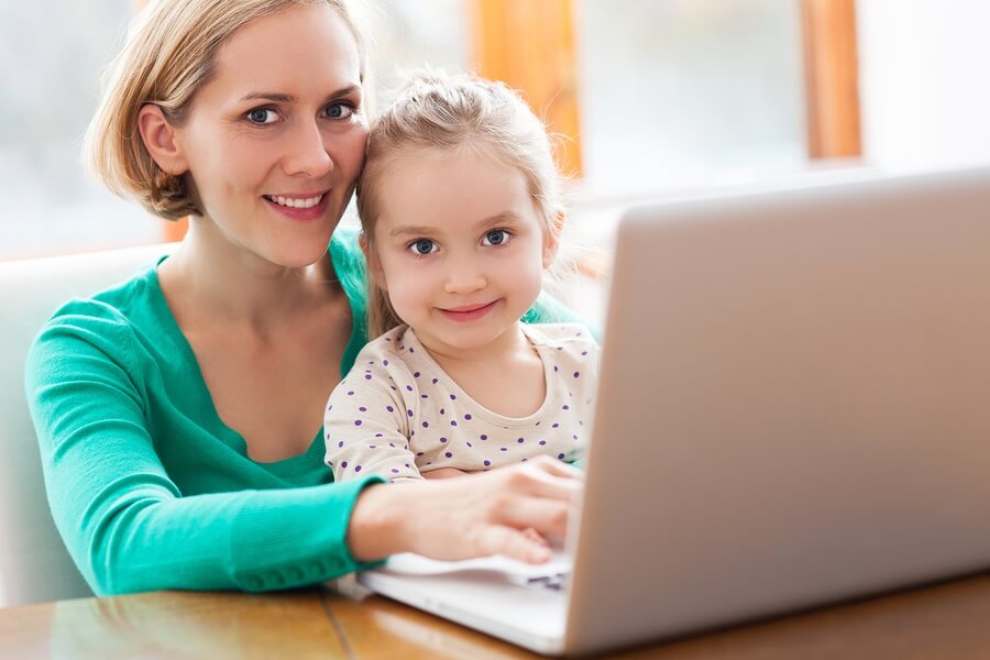 Mother and daughter sitting at desk using laptop