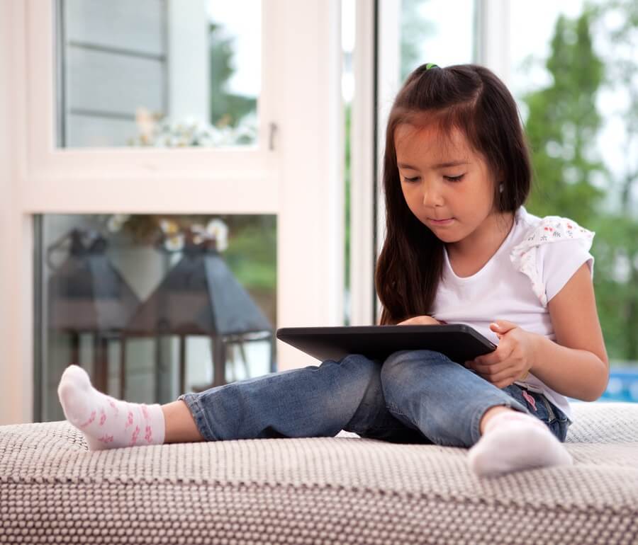 Young girl sitting on couch playing with tablet computer