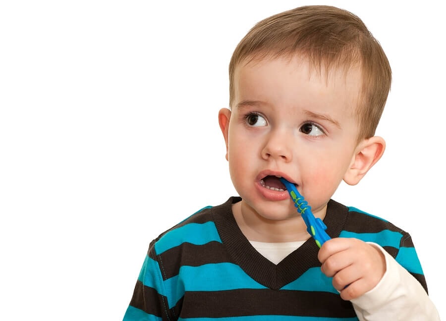 Close up o toddler brushing his teeth against white back drop.