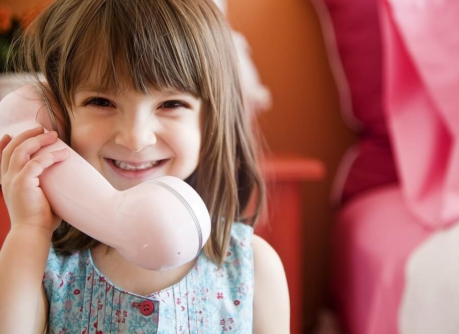 Close up of young girl talking on big pink phone.