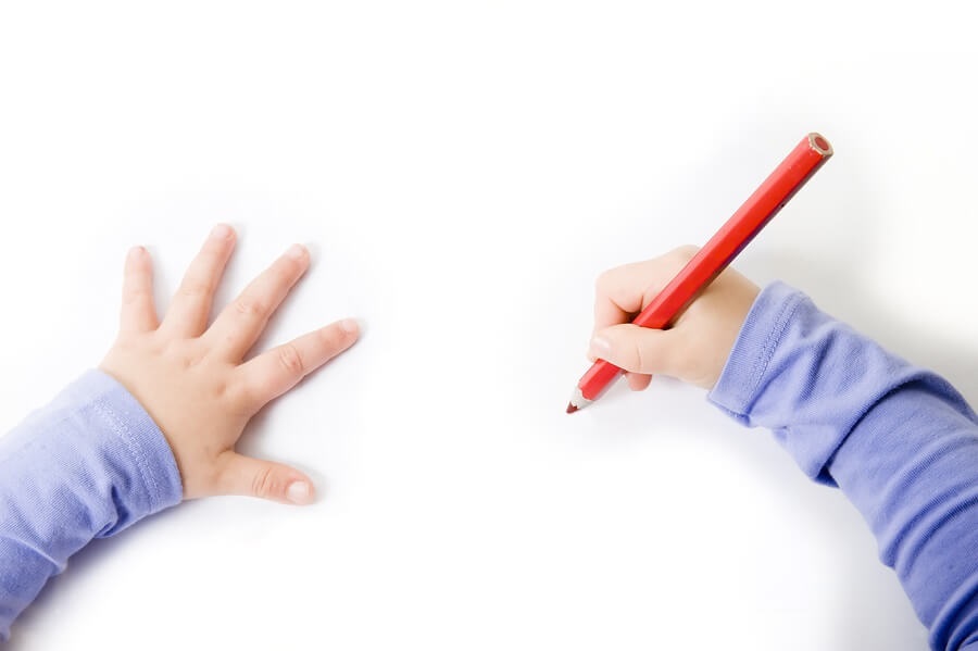 Child's hand drawing on white paper with pencil.