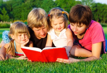 Smiling family laying on grass reading book