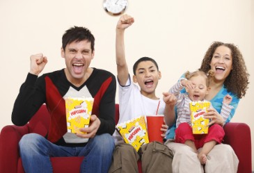 Happy family sitting on couch, cheeroing and eating popcorn