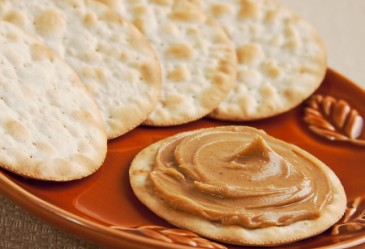 Cracker with peanut on plate with crackers in background.