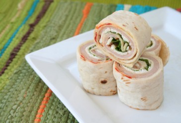 Turkey wrap cut into rolls, stacked on plate against place mat backdrop.